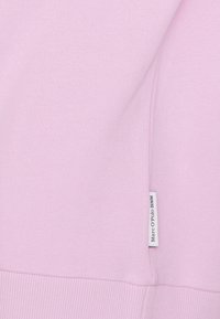 Light pink sweatshirt with a textured fabric and ribbed hem. Features a white tag on the side with "Marc O'Polo DENIM" printed.