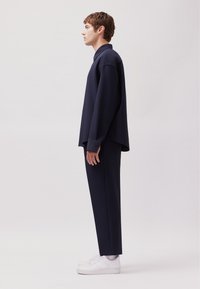 Camicia e pantaloni over-size blu navy con una silhouette rilassata, abbinati a sneaker bianche. Il tessuto è liscio, con maniche lunghe e colletto abbottonato.