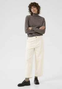 Licht beige, wijde corduroy broek met hoge taille en zijzakken, gecombineerd met een aansluitende donkerbruine coltrui. Zwarte loafers.
