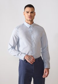 Lichtblauw overhemd met lange mouwen en een gespreide kraag, met een gladde textuur en witte knopen, gecombineerd met donkerblauwe broek.