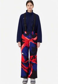 Pantaloni da sci con motivo astratto in rosso, blu e nero e bretelle nere regolabili. Abbinati a una giacca in pile blu navy con cerniera.