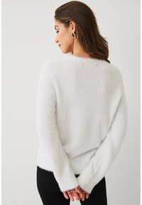 Witte, pluizige trui met een ontspannen pasvorm, lange mouwen en geribbelde manchetten. Eenvoudig ontwerp, zachte textuur, geschikt voor casual draagstijl.