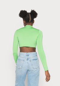 Top cropped verde de manga longa com um design ajustado e textura suave, combinado com jeans claros de cintura alta e desgastados.