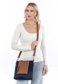 Borsa a tracolla blu navy in nylon con una tasca frontale in pelle marrone, dotata di zip e tracolla regolabile. Texture liscia con hardware in metallo.