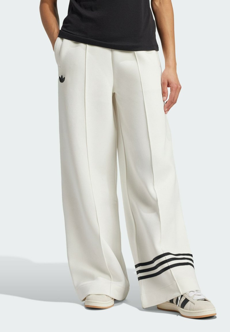 Białe spodnie o szerokich nogawkach z zakładkami, z czarnym logo Adidasa i trzema czarnymi paskami wzdłuż dolnej krawędzi. Gładki materiał o eleganckim kroju.