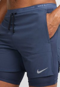 Shorts de running Nike en azul marino oscuro, con cintura ajustable mediante cordón, bolsillos laterales y un logo reflectante en la pierna izquierda. Tejido texturizado.