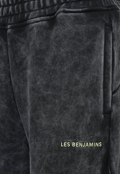 Schwarze, strukturierte Jogginghosen mit einem elastischen Bund und einer seitlichen Tasche. Mit dem grünen gestickten Markennamen "LES BENJAMINS" auf der Vorderseite.