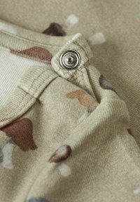 Beżowa tkanina o teksturowanym wykończeniu z wielokolorowym abstrakcyjnym wzorem. Srebrny zatrzask zdobi kołnierz złożony na pół.