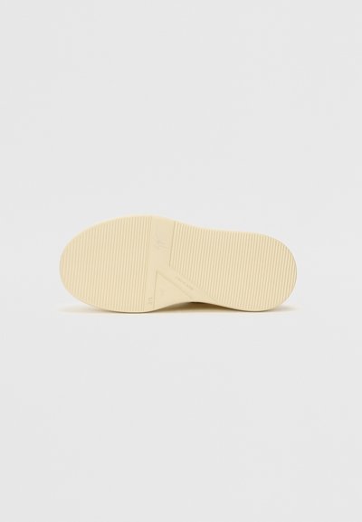 Rubber shoe sole, cream-colored with horizontal and vertical grooves. Features a slight heel and embossed logo on the side.