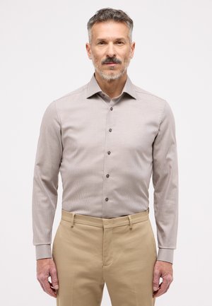Beige karierte Langarmbluse mit einem klassischen Kragen, braunen Knöpfen und Manschetten. Kombiniert mit beigen Hosen mit flachem Vorderteil.