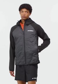 Veste noire isolée avec fermeture éclair sur le devant, col montant et manches contrastées. Présente une finition mate, un logo sur la poitrine et des poches latérales.