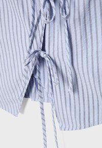 Tissu bleu clair avec de fines rayures verticales foncées, présentant deux nœuds attachés sur une ouverture fendue.