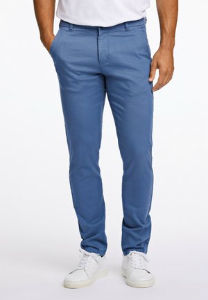 Blaue Chinos mit glatter Textur und schlankem Schnitt, ausgestattet mit frontalen Taschen und einem flachen Frontdesign, kombiniert mit weißen Sneakers.