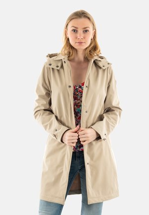 Beige waterproof jacket with a hood, snap buttons, and pockets. Worn over a colorful floral top, paired with blue jeans. Smooth texture.