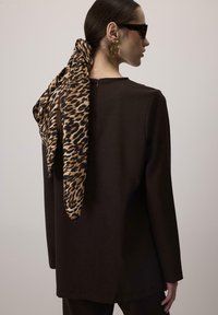 Smeđa duga rukava majica s okruglim izrezom, s maramom u leopard uzorku vezanom u kosi. Vidljive zlatne naušnice. Glatka tekstura tkanine.