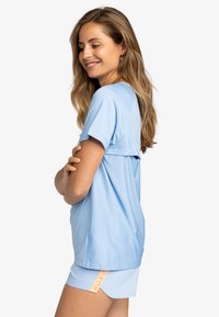 Lichtblauw sporttop met korte mouwen en een relaxte pasvorm, gecombineerd met bijpassende shorts. De shorts hebben een logo-label in contrasterende kleur.