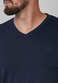 Granatowa koszulka typu v-neck z krótkim rękawem, wykonana z miękkiego materiału, z subtelnym logo s.Oliver na piersi, gładka faktura i luźny krój.
