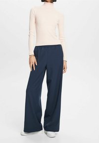 Top de cuello alto de color rosa claro con diseño de canalé, combinado con pantalones amplios de pierna ancha de color azul oscuro y corte holgado. Diseño sencillo con cintura elástica y zapatos blancos.