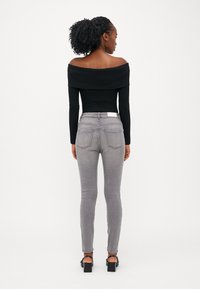 Juodas off-the-shoulder banguotas augšas derinamas su priglundančiomis pilkomis džinsomis. Apranga pasižymi lygia tekstūra ir subtiliu siuvimo detalių akcentu.