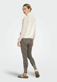 Sudadera de forro polar color beige claro con cuello alto, combinada con leggings marrones con estampado y zapatillas marrones. Textura suave y ajuste atlético.