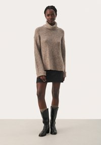 Beiger Rollkragenpullover mit lockerer Passform, getragen über einem schwarz-karierte Rock. Schwarze knielange Lederstiefel. Weiche Textur, entspannter Design.