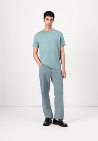 Světle modré bavlněné tričko s kulatým výstřihem, nošené se světle modrými džíny rovného střihu a černými botami; minimalistický design, bez výrazných vzorů.