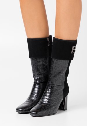 Stivali neri a metà polpaccio con texture effetto coccodrillo, tacchi a blocco, polsini in suede ripiegabili, cerniere laterali e logo metallico a forma di "B" sul polsino esterno.