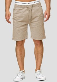 Shorts en coton beige avec une taille élastique et un cordon de serrage. La taille présente un logo imprimé. Fini avec un ourlet droit.