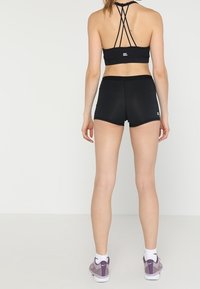 Svart atletisk crop top med korsade axelband, tillsammans med svarta shorts. Materialet är mjukt, med en figurnära design och minimal logo.