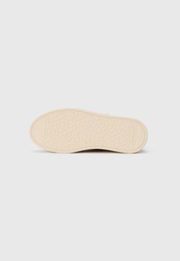 Talpa bej cu un model de profil hexagonal și imprimația "STEVE MADDEN" pe un fundal alb.