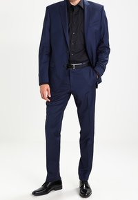 Completo blu navy con una vestibilità su misura, caratterizzato da un blazer mono colore, una camicia nera elegante e scarpe nere lucide. Tessuto morbido e design della revers appuntito.