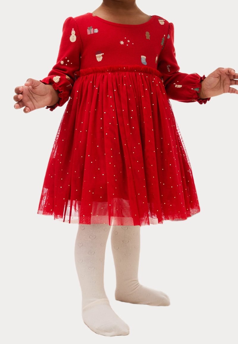 Enfant portant une robe rouge à manches longues avec des motifs sur le thème des fêtes et des collants blancs avec de subtils dessins de cœurs.