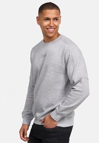 Szary sweatshirt z okrągłym dekoltem, raglanowymi rękawami i małym logo na klatce piersiowej. Teksturowana tkanina, ściągacze u rękawów oraz na dole.