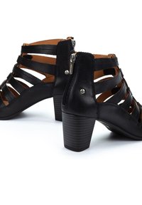 Botines negros de cuero con correas recortadas, puntera redonda y tacón apilado. Cuenta con una cremallera lateral y un forro interior suave.