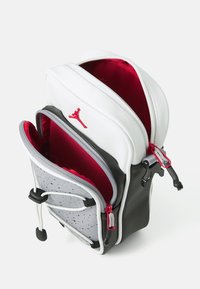 Zaino con esterno bianco e nero, interno rosso, accenti grigi perforati, doppie cerniere e un logo rosso prominente sul davanti.