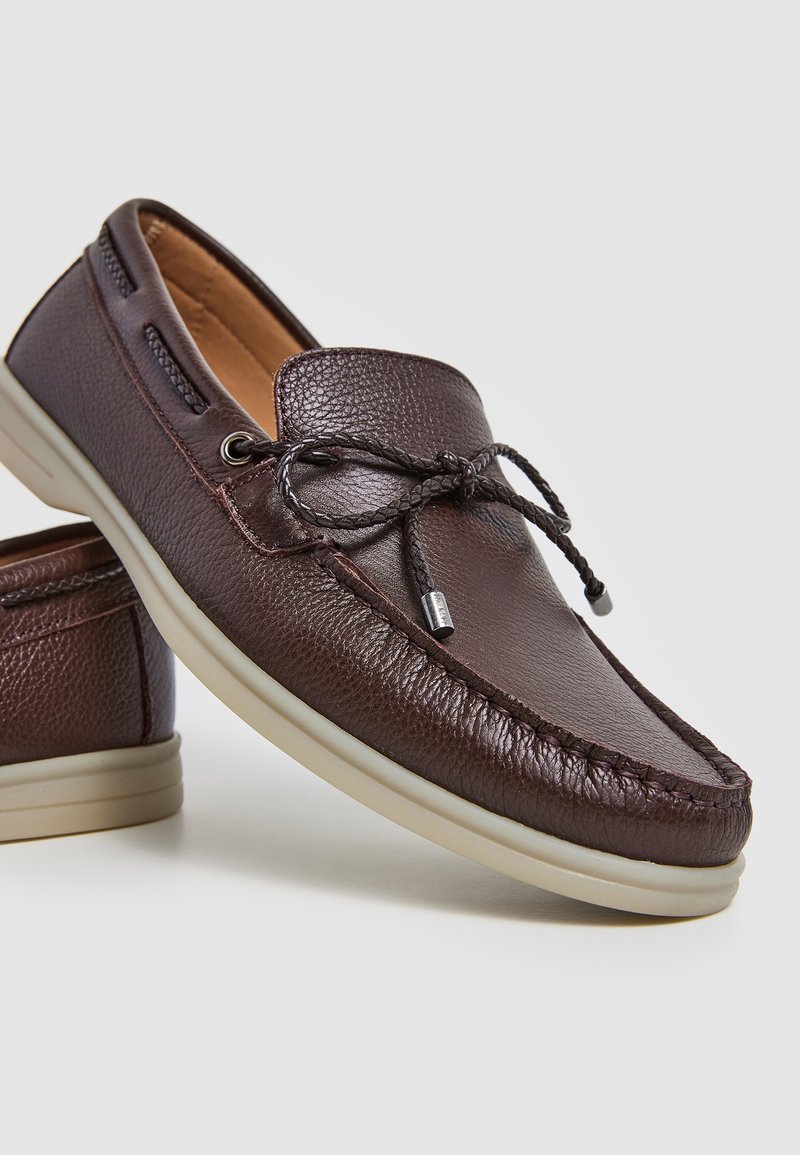 Mocassins en cuir marron avec finition texturée, détail de lacets et semelle en caoutchouc beige. Bout arrondi, accents de couture et ouvertures latérales.