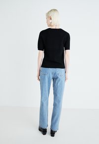 Black textured short-sleeve top paired with light blue high-waisted denim jeans and black block-heeled shoes, shown from the back.