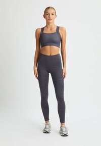 Sujetador deportivo gris con tirantes anchos combinado con leggings gris de talle alto que presentan un sutil patrón geométrico, estilizados con zapatillas de correr.