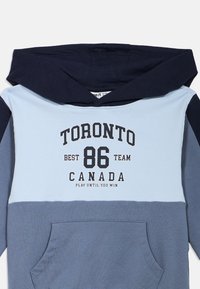 Hoodie in tinten blauw met een buidelzak, met de tekst "TORONTO BEST 86 TEAM CANADA" in zwart en wit.