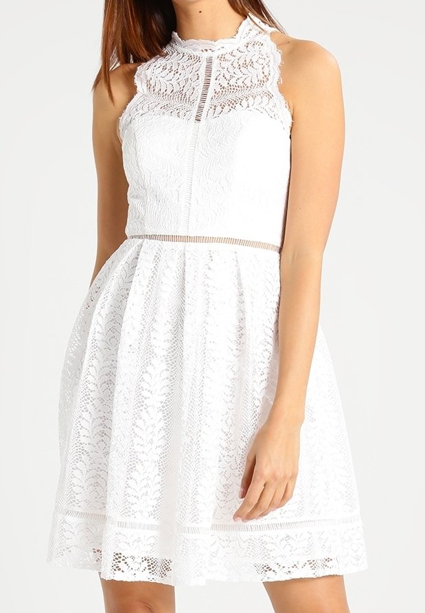 Vitt spetsklänning med hög hals, ärmlös design, texturerade blommönster och en utsvängd kjol med en subtil fålldetalj.