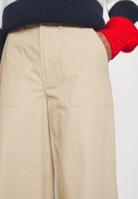 Béžové bavlněné kalhoty s volným střihem, které mají dvě boční kapsy a viditelné švy. Látka má hladkou strukturu.