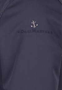 Marinejakke med et broderet ankerlogo og teksten "DreiMaster" i sølvtråd. Glat tekstur, professionelt design, minimalt detalje.