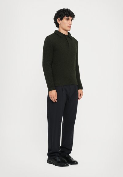 Dunkelgrüner, strukturierten Strickpullover mit Kragen, kombiniert mit dunklen Hosen und schwarzen Schuhen. Das Design verfügt über lange Ärmel und eine taillierte Passform.