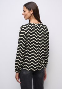 Blusa de chevrón en negro y crema con mangas largas, cuello redondo y detalle de botones en la parte trasera. Textura suave y lisa.