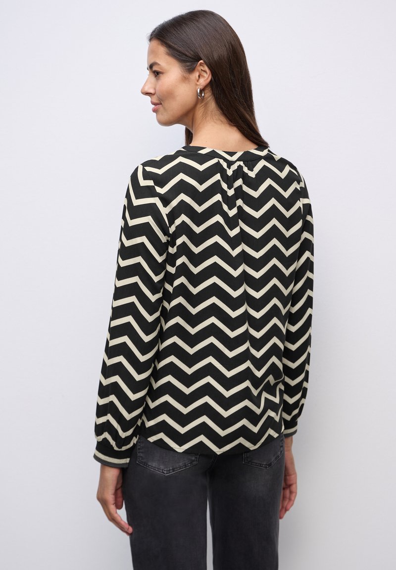 Blusa de chevrón en negro y crema con mangas largas, cuello redondo y detalle de botones en la parte trasera. Textura suave y lisa.