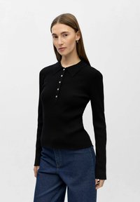 Ribbestrikket svart langermet topp med krage og knappet stolpe, kombinert med høytlivs blå denimbukser. Glatt tekstur, tettsittende design.