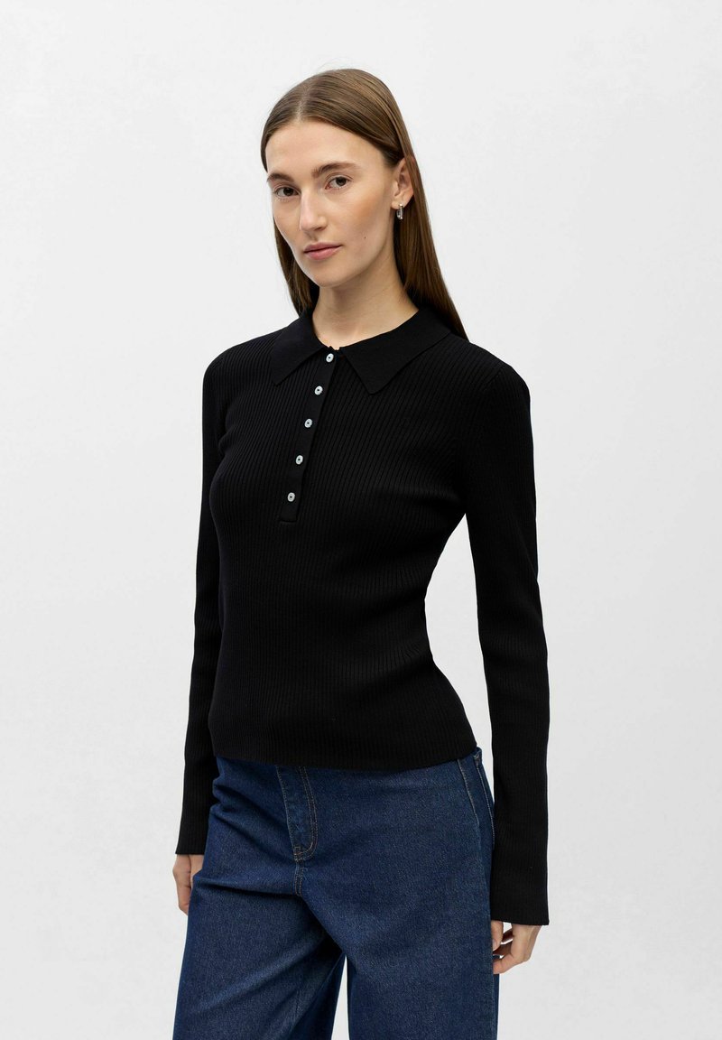 Ribbestrikket svart langermet topp med krage og knappet stolpe, kombinert med høytlivs blå denimbukser. Glatt tekstur, tettsittende design.