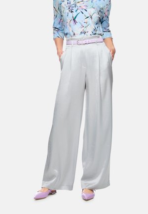Woman wearing wide-leg silver trousers, a floral blue top with three-quarter sleeves, lilac belt, and matching lilac pointed flats.