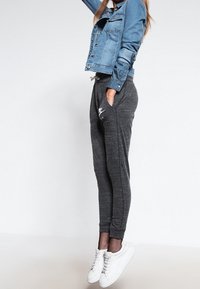 Chaqueta de denim con bolsillos, color azul claro; joggers grises con un acabado texturizado y bolsillos laterales; zapatillas blancas; detalle de red en el tobillo.