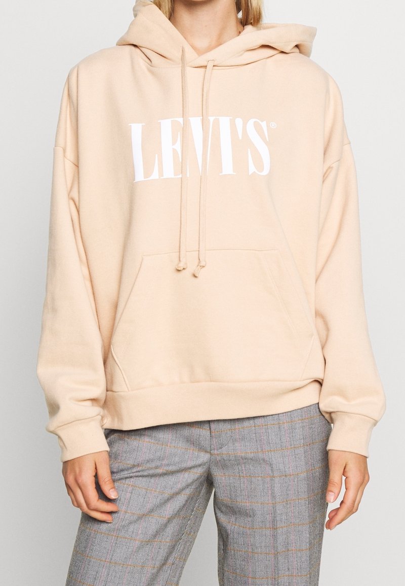 Felpa beige con logo bianco "LEVI'S®". Presenta un cappuccio con cordino, tasca a marsupio frontale e polsini a costine. Materiale morbido e vestibilità rilassata.